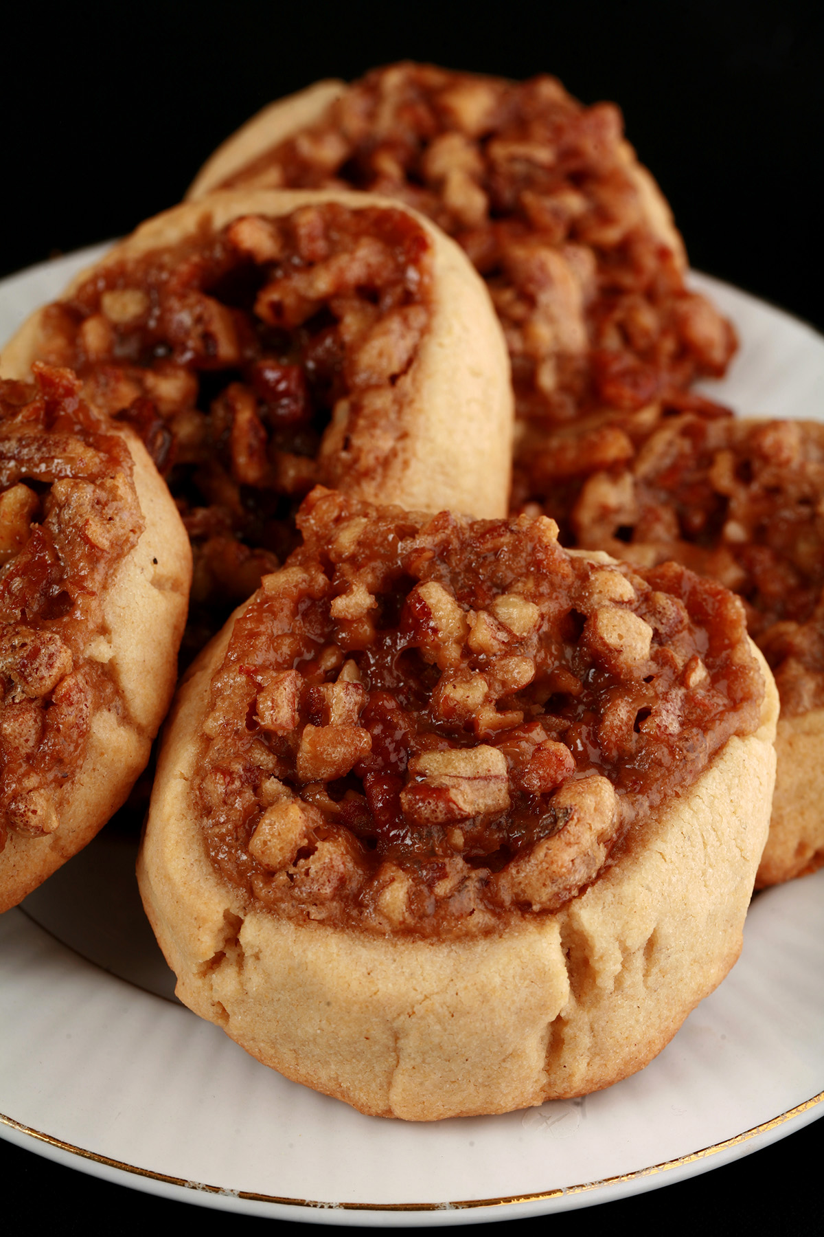 Several Gluten-Free Pecan Pie cookies on a white plate. They are golden brown, with a pecan and brown sugar topping.
