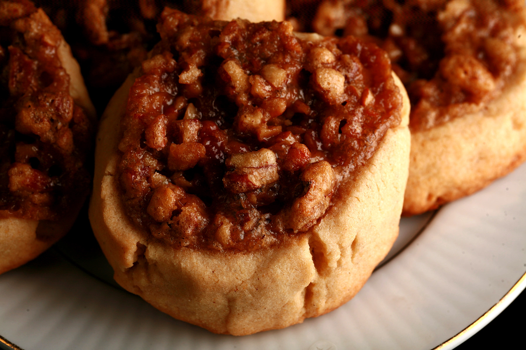Several Gluten-Free Pecan Pie cookies on a white plate. They are golden brown, with a pecan and brown sugar topping.