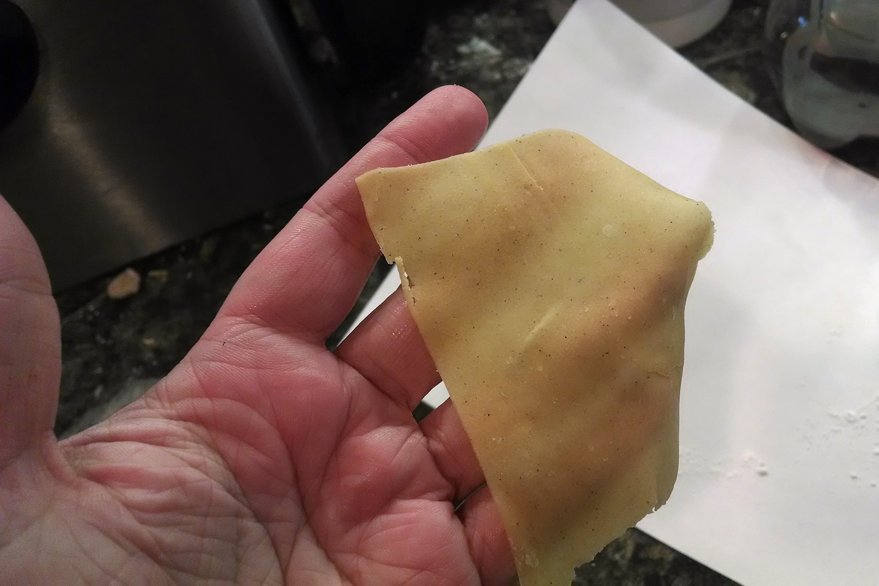 A hand holds up a piece of thinly rolled gluten-free dough.