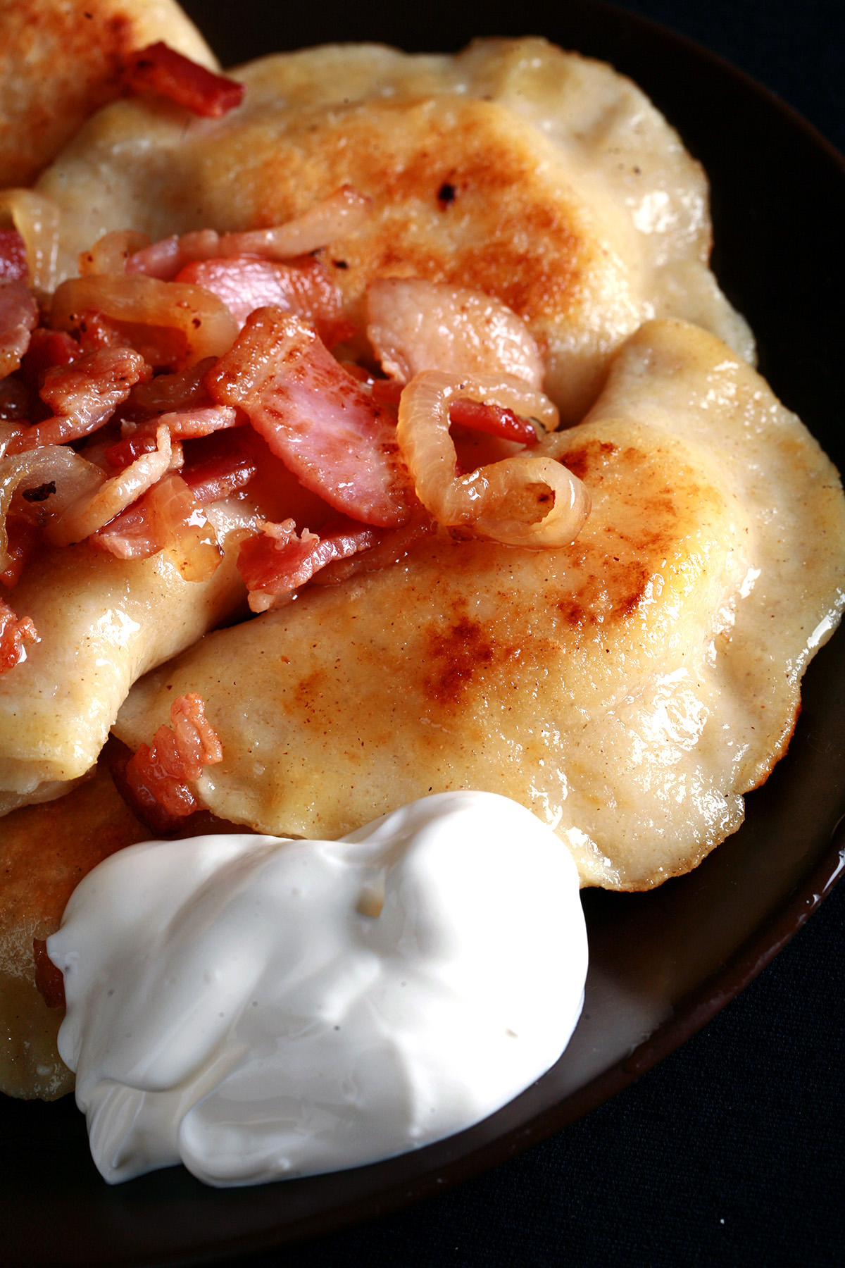 A plate of gluten-free pierogi, topped with bacon, fried onions, and sour cream.