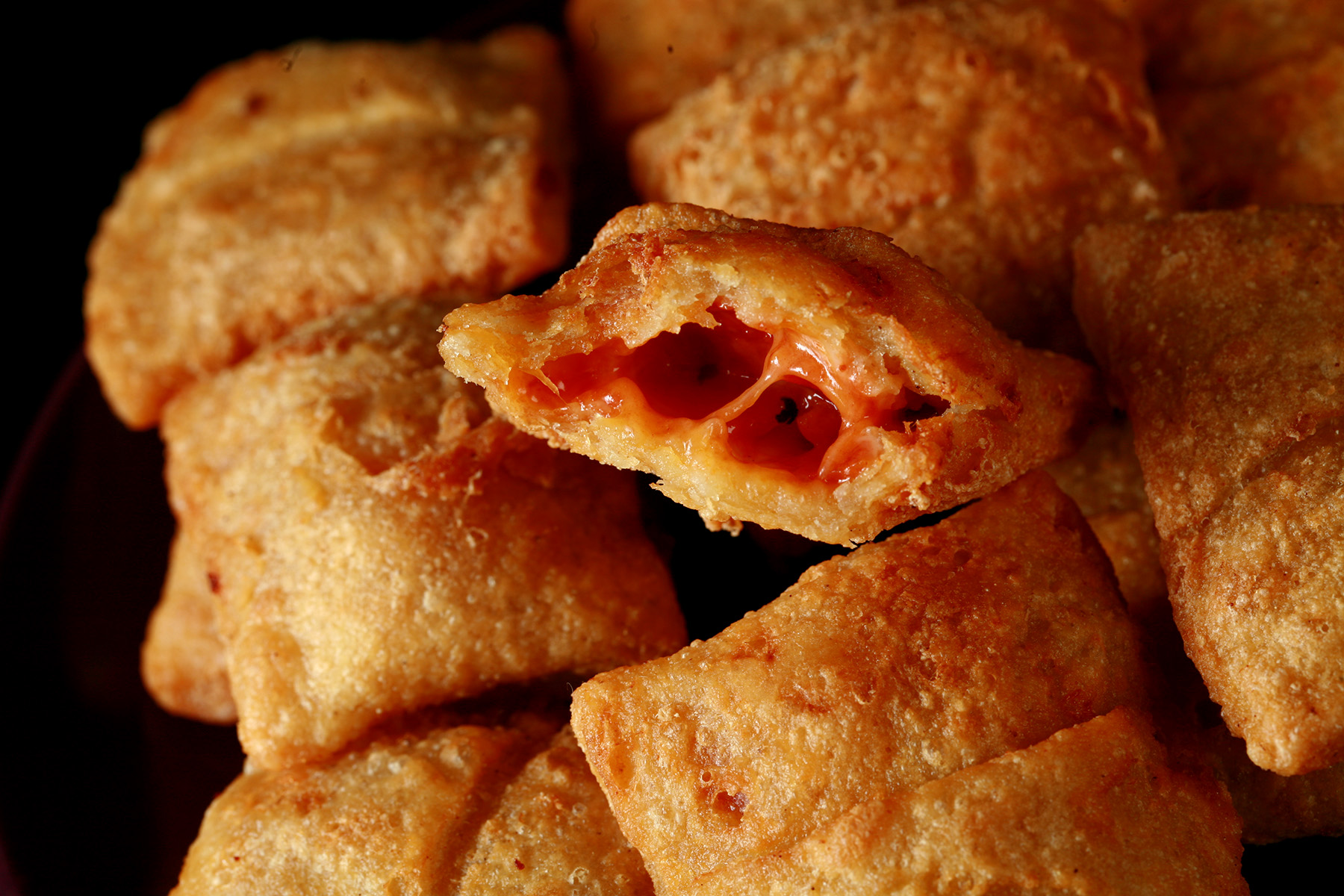 A plate with a pile of gluten-free pizza bites. One has been cut in half to show its pizza filling.