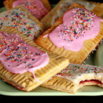 A plate of toaster pastries made from this gluten-free poptarts recipe. They are frosted with pink and white icing, and topped with coloured sprinkles.