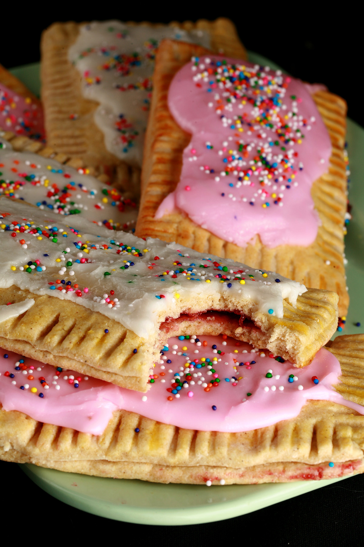 A plate of gluten free homemade poptarts, frosted with pink and white icing, topped with coloured sprinkles.