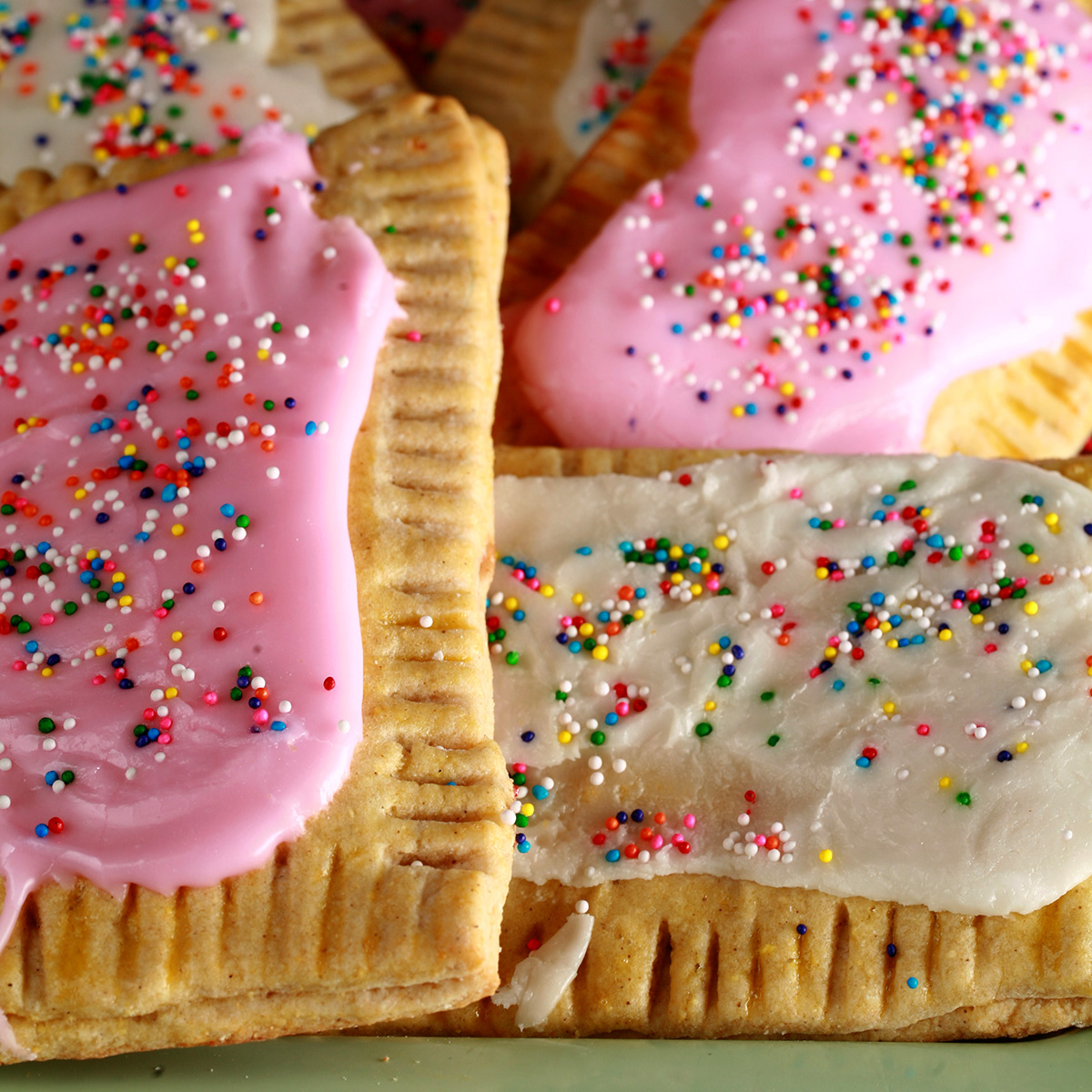 A plate of gluten free homemade poptarts, frosted with pink and white icing, topped with coloured sprinkles.
