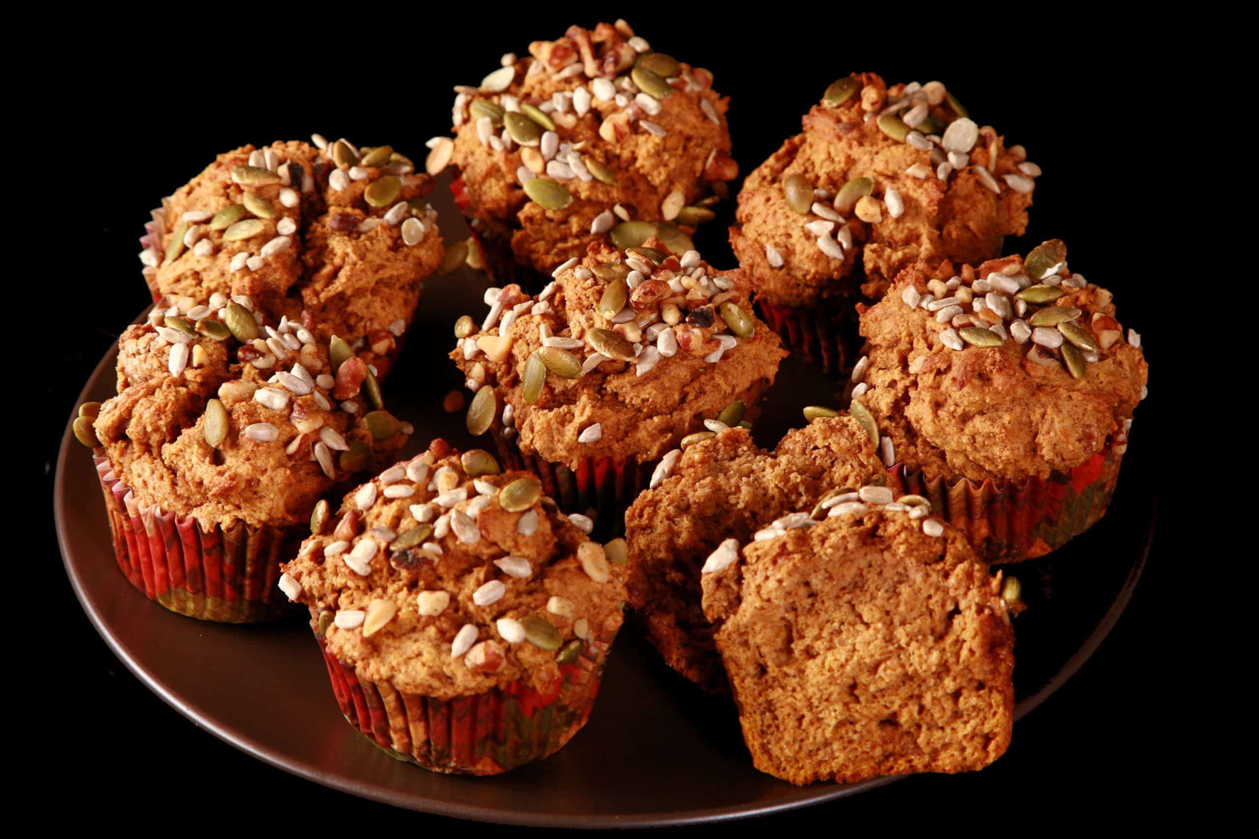 A plate of gluten-free pumpkin muffins, all topped with a mix of seeds and nuts.