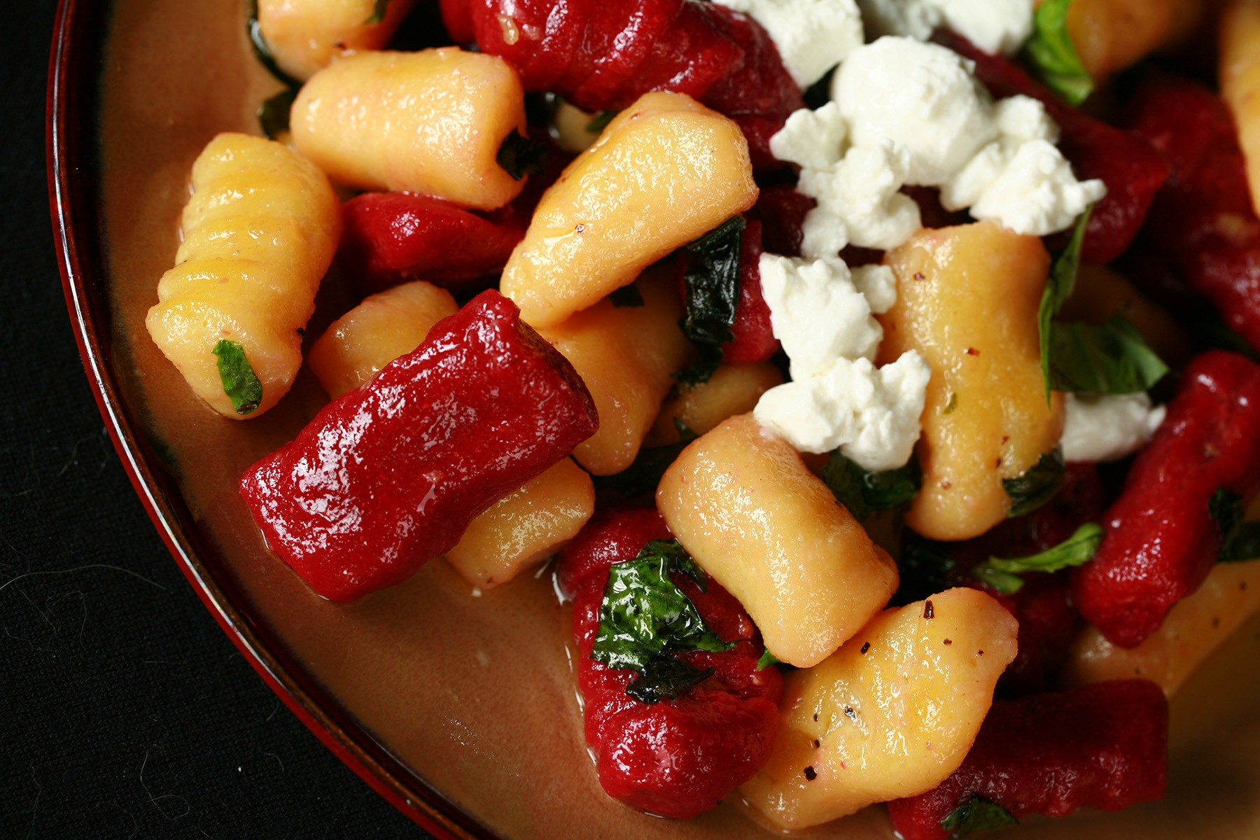 A plate of red and yellow roasted beet gnocchi. It's topped with crumbled goat cheese and fresh basil.
