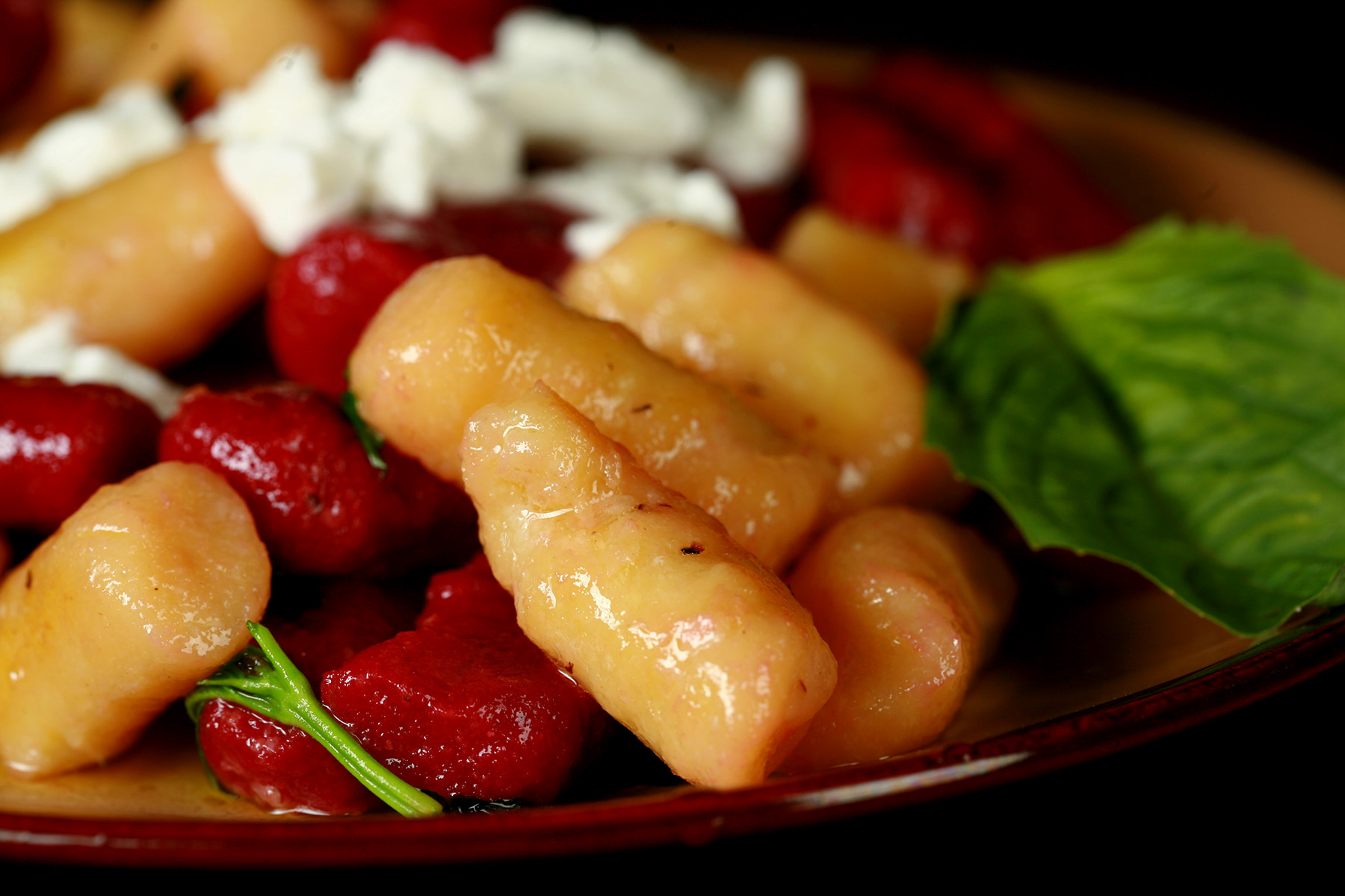 A plate of red and yellow roasted beet gnocchi. It's topped with crumbled goat cheese and fresh basil.