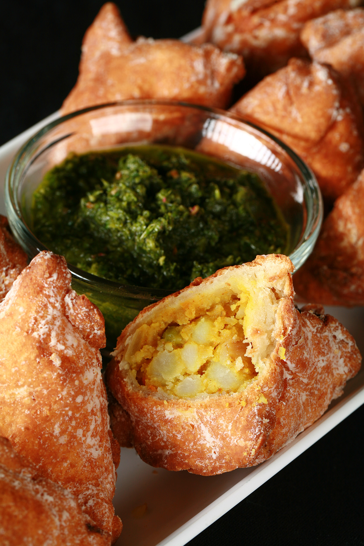 Several Gluten-Free Samosas on a tray, surrounding a small bowl of cilantro chutney.