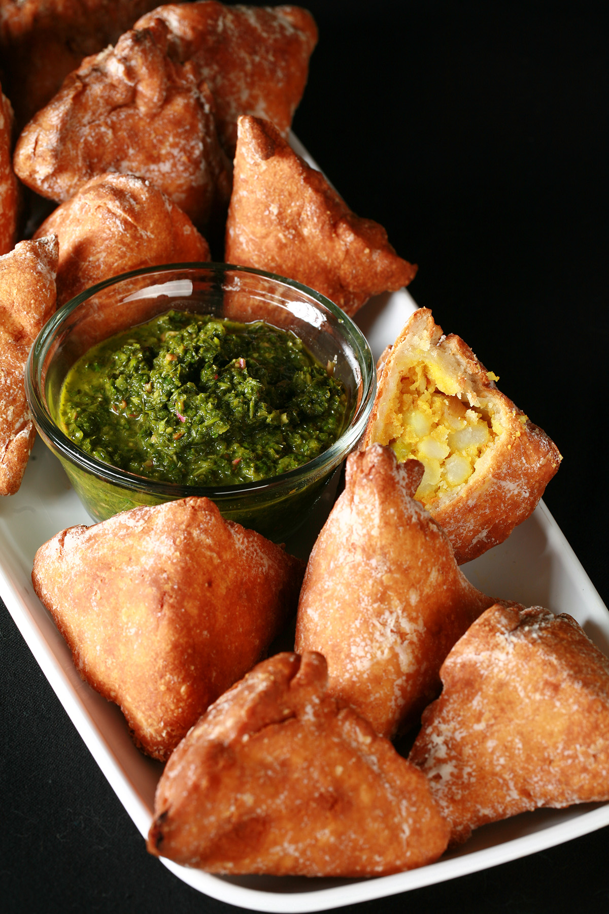 Several Gluten-Free Samosa on a tray, surrounding a small bowl of cilantro chutney.