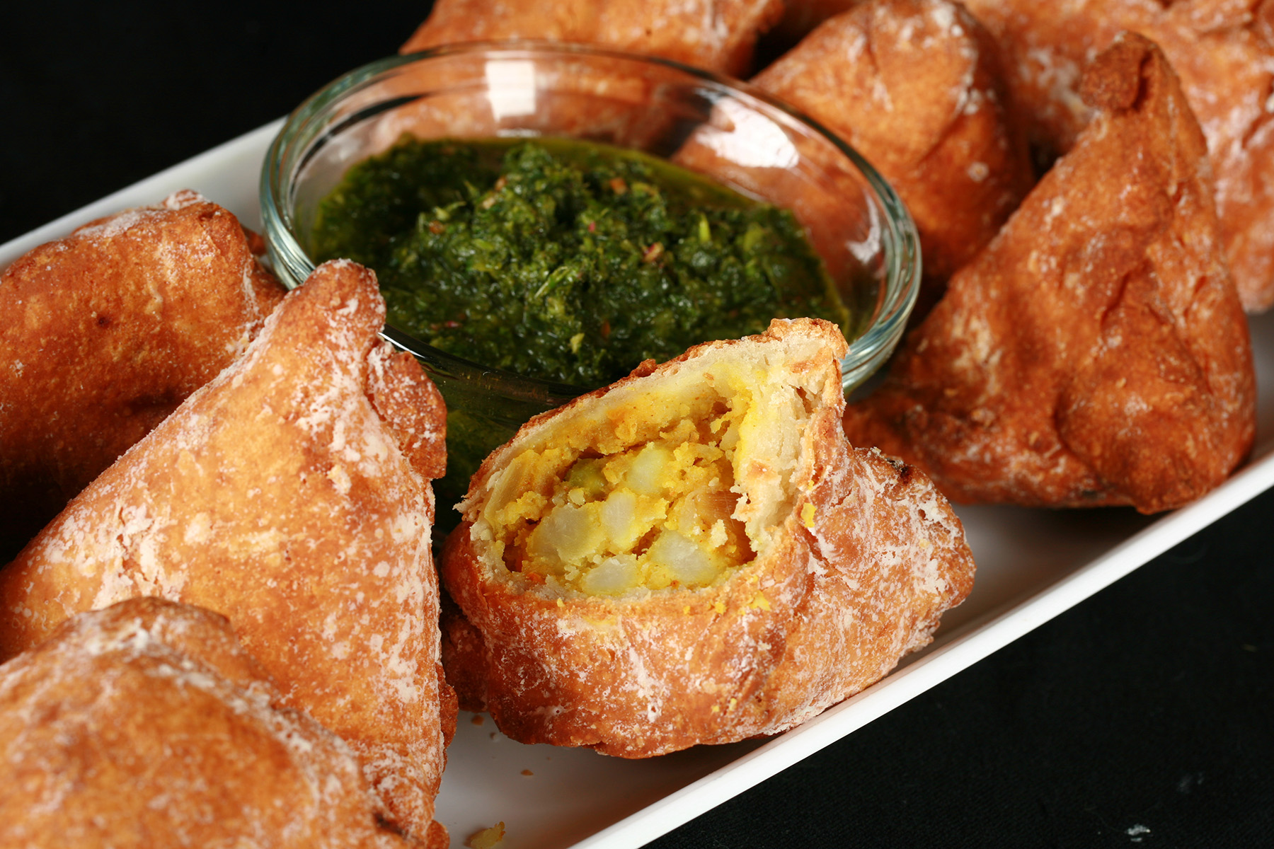 Several Gluten-Free Samosa on a tray, surrounding a small bowl of cilantro chutney.