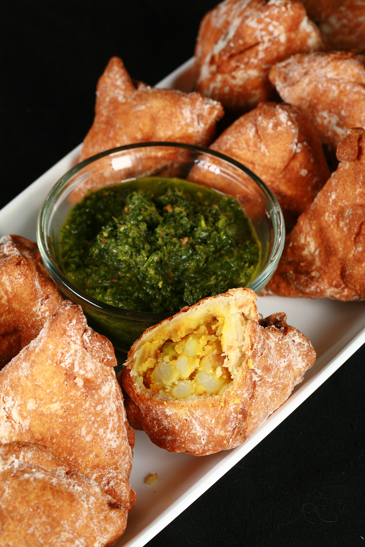 Several Gluten-Free Samosa on a tray, surrounding a small bowl of cilantro chutney.