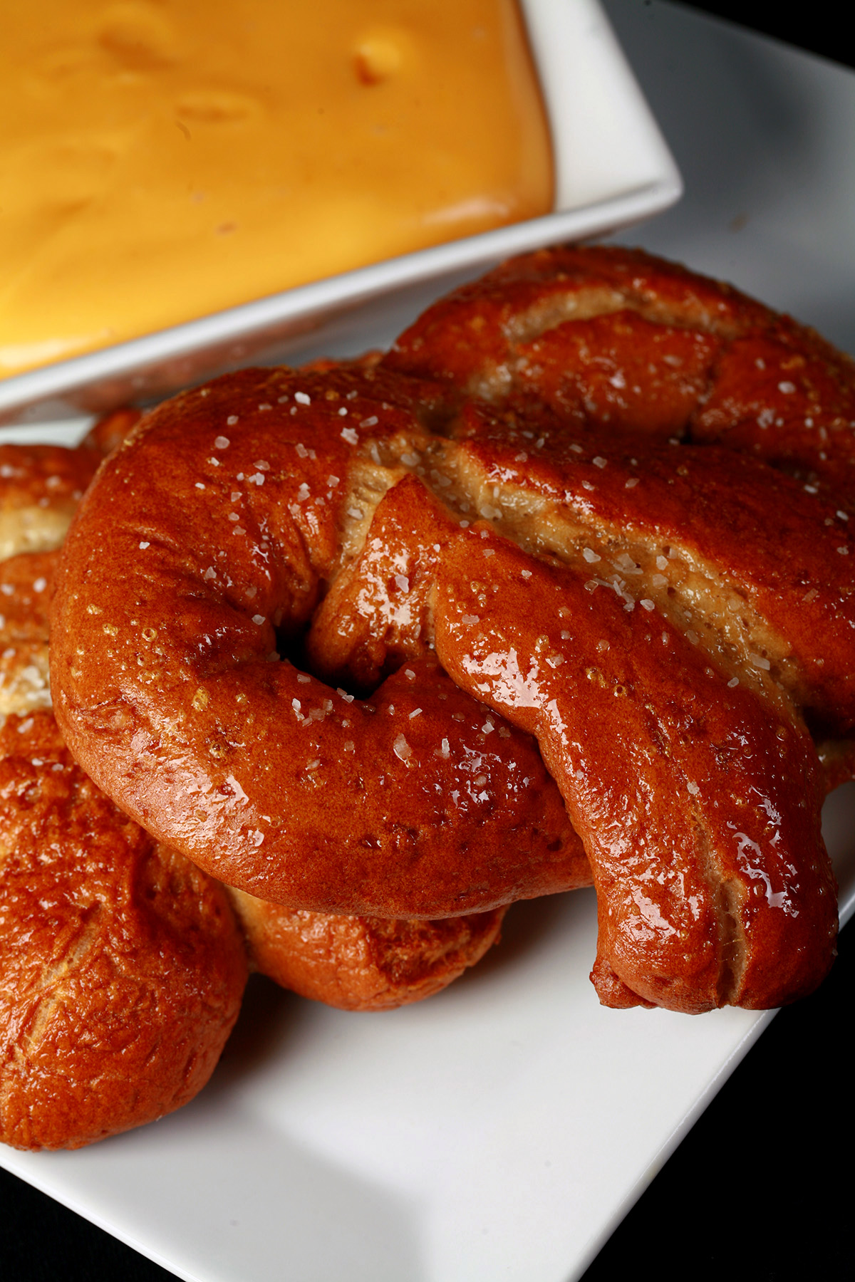 2 soft gluten-free pretzels on a plate, beside a bowl of mustard-cheddar dip.