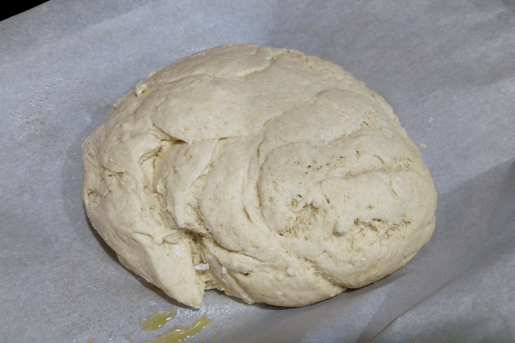 A ball of gluten-free dough on a parchment lined work surface.