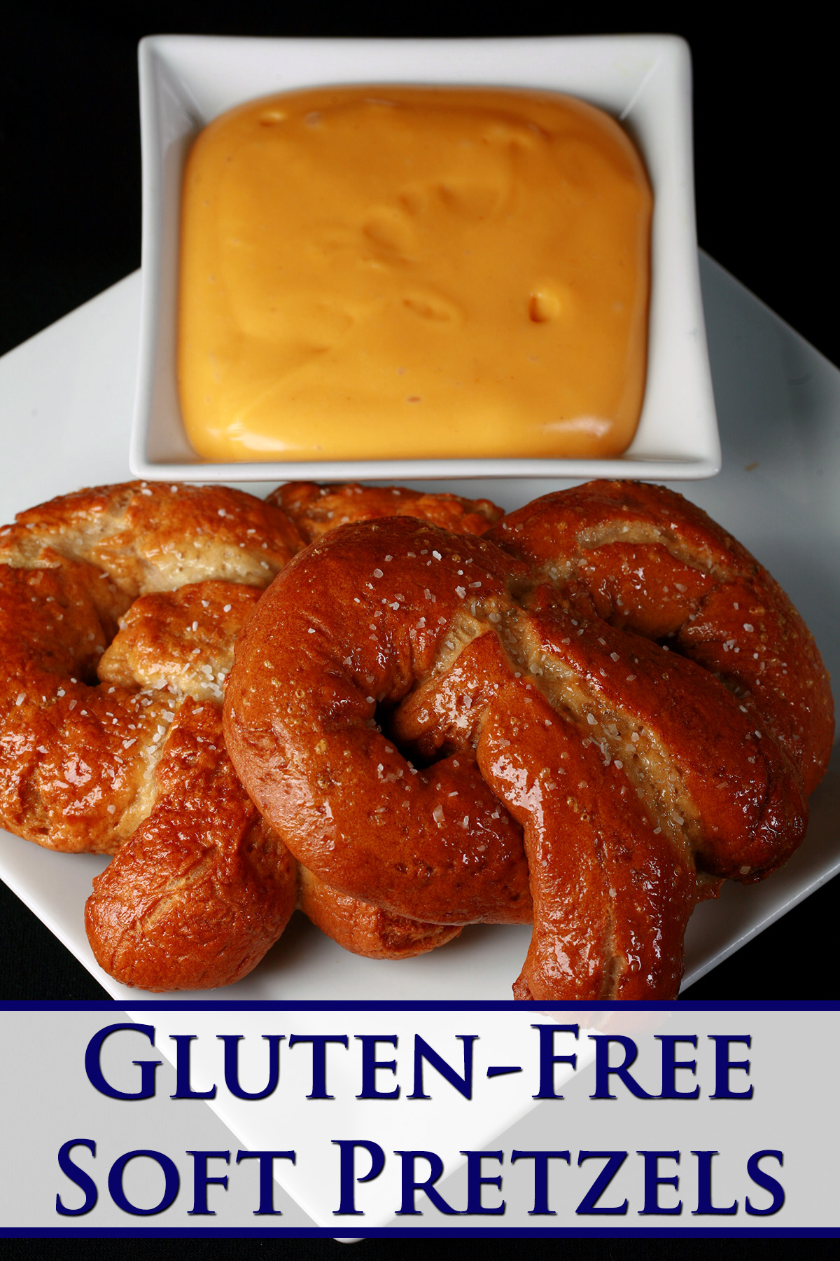 2 gluten-free soft pretzels on a plate, beside a bowl of mustard-cheddar dip.