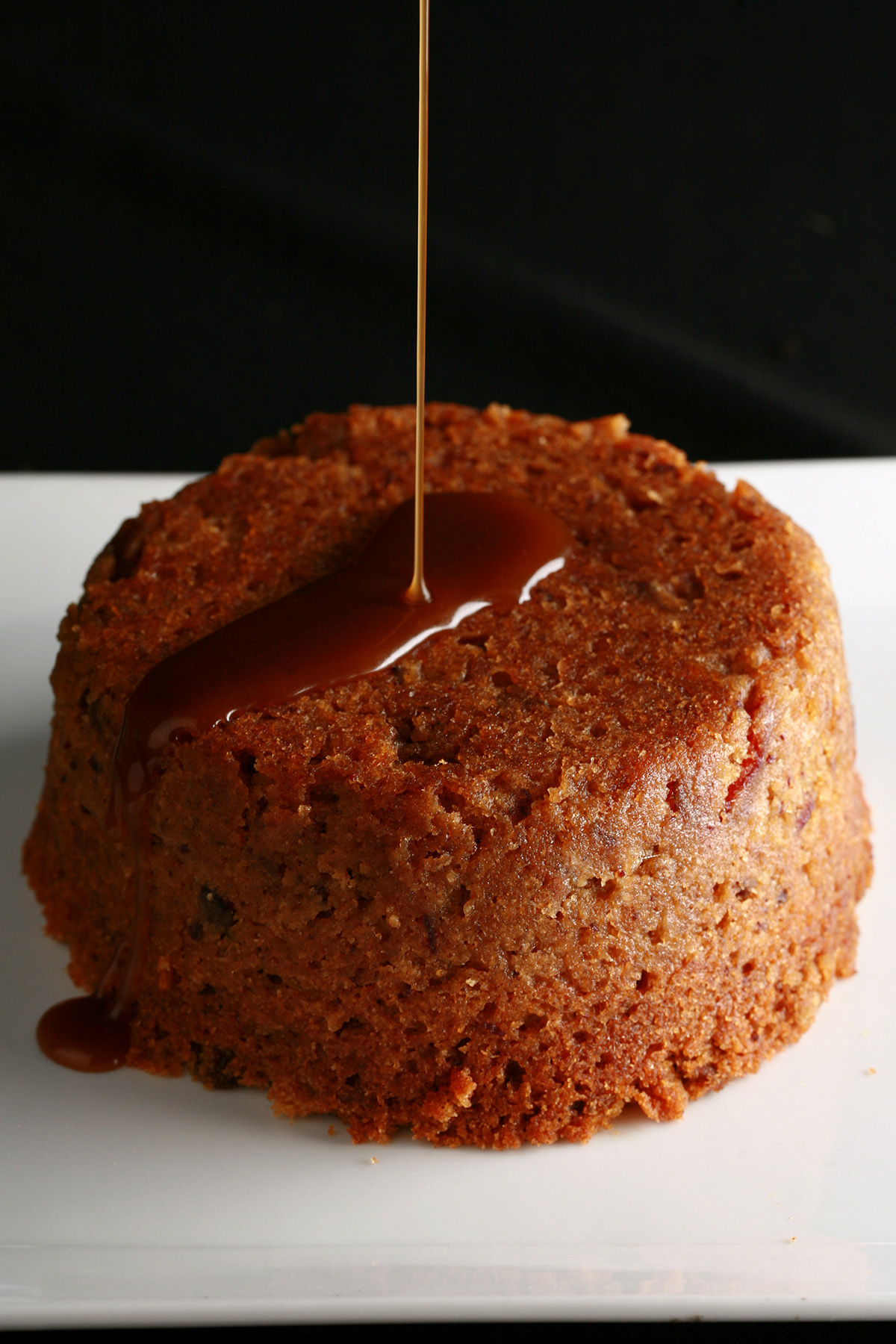 A gluten free sticky toffee pudding with toffee sauce being poured over it.
