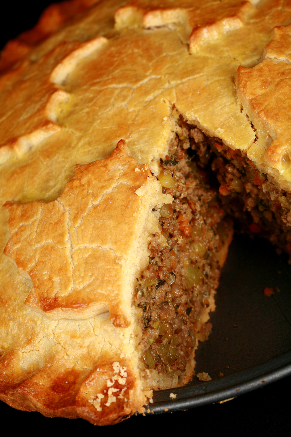 A golden brown gluten-free tourtiere meat pie, with a maple leaf design on top.. There is a section cut out of it