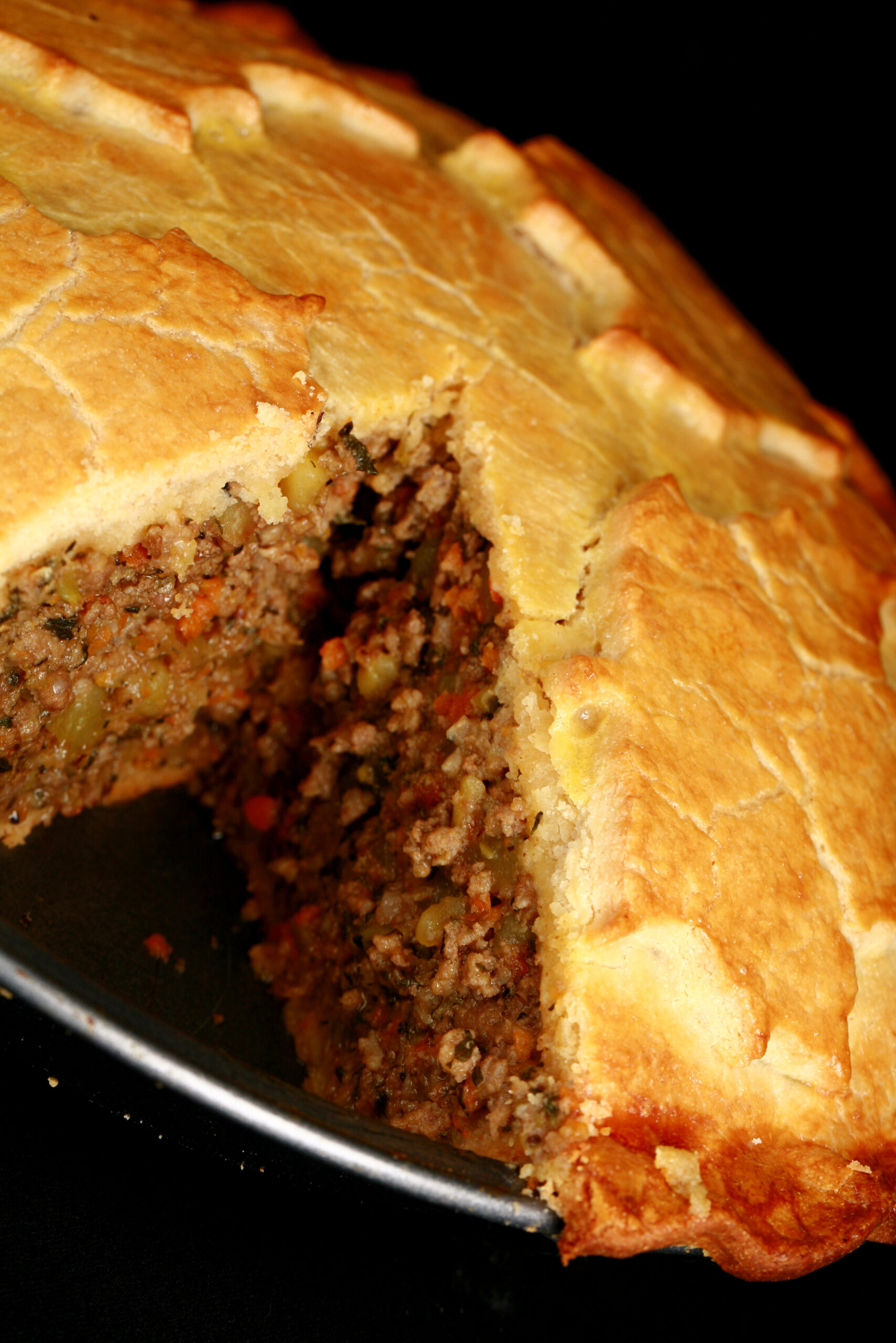 A golden brown baked meat pie, with a maple leaf design on top. There is a section cut out of it.