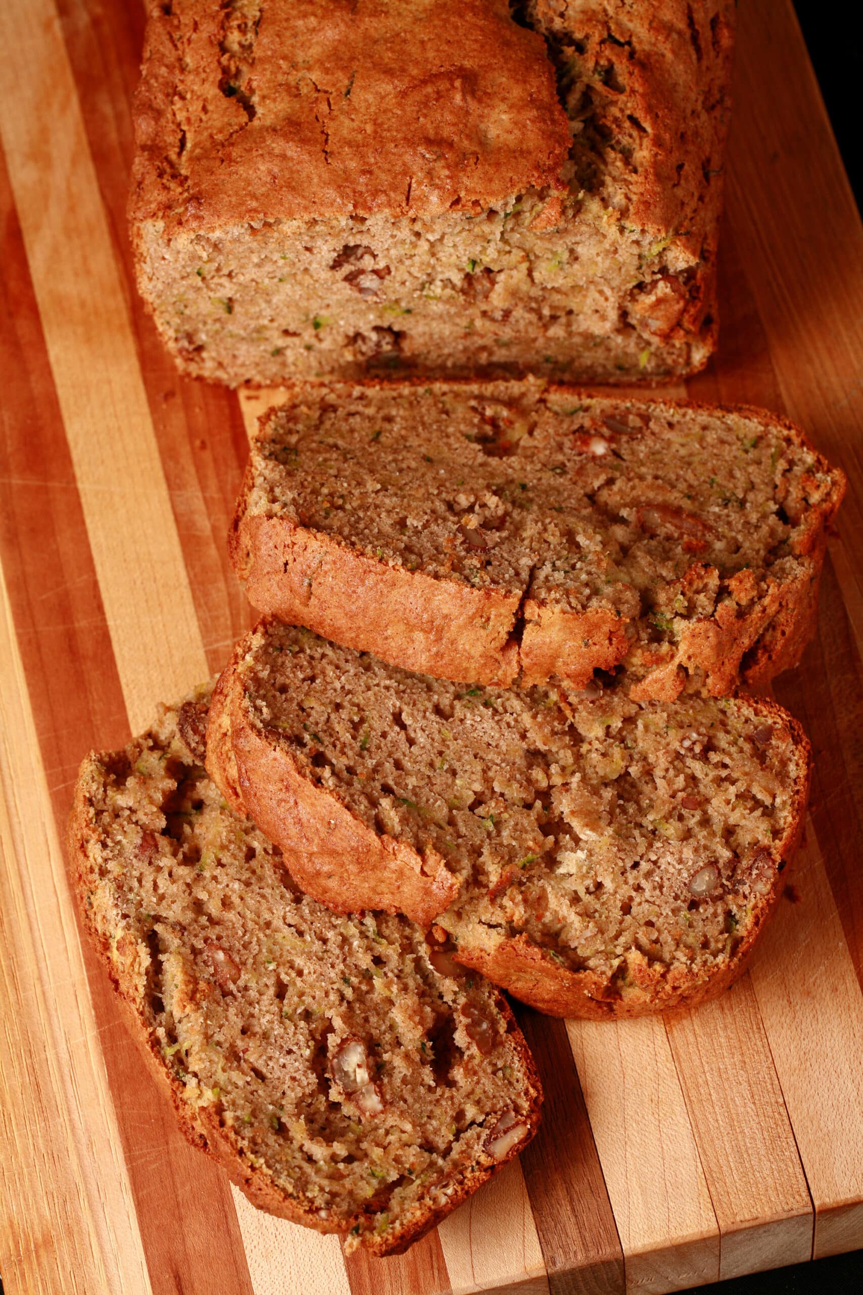 A sliced loaf of gluten-free zucchini bread on a wooden cutting board.