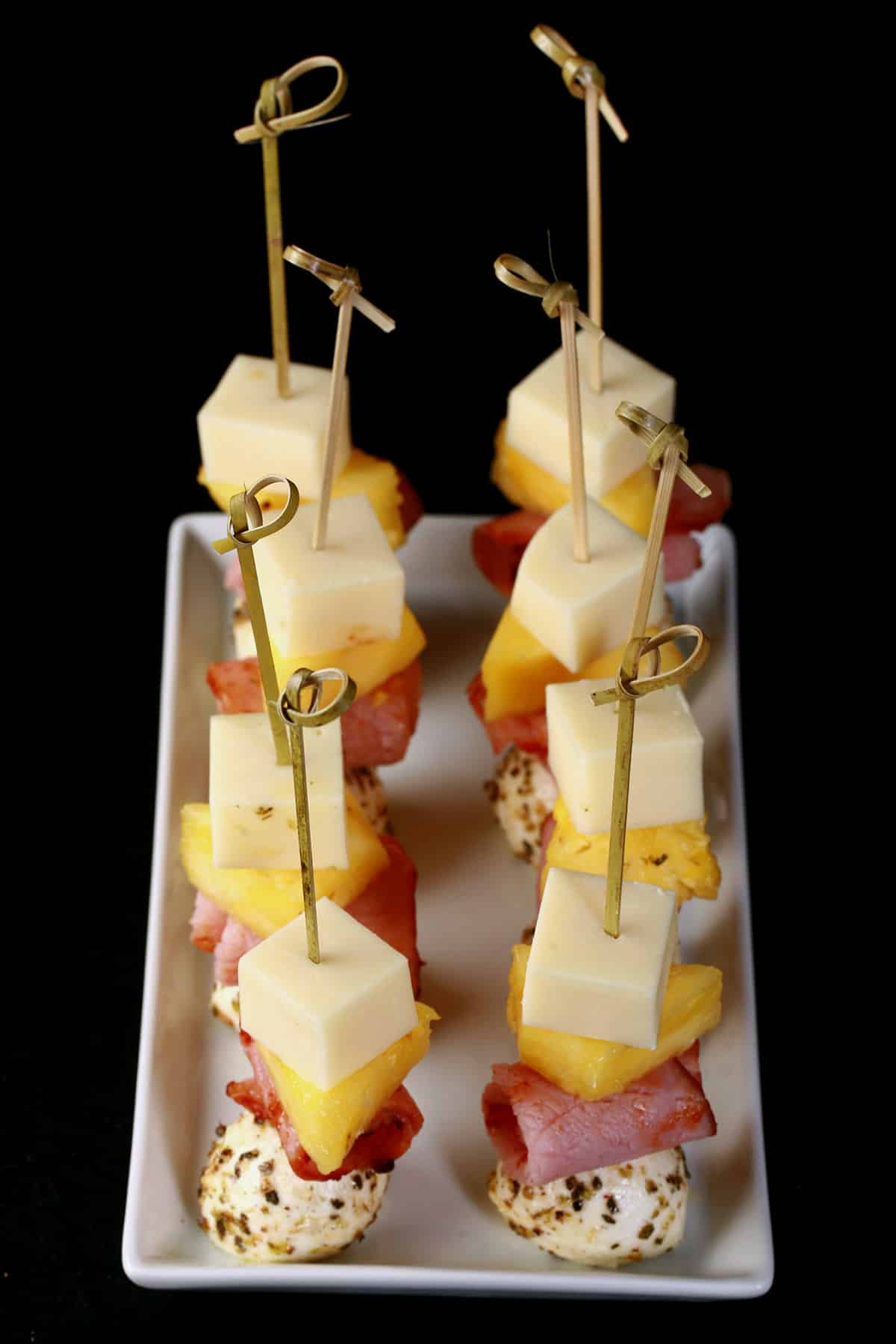 A tray of hawaiian pizza themed ham and pineapple skewers.