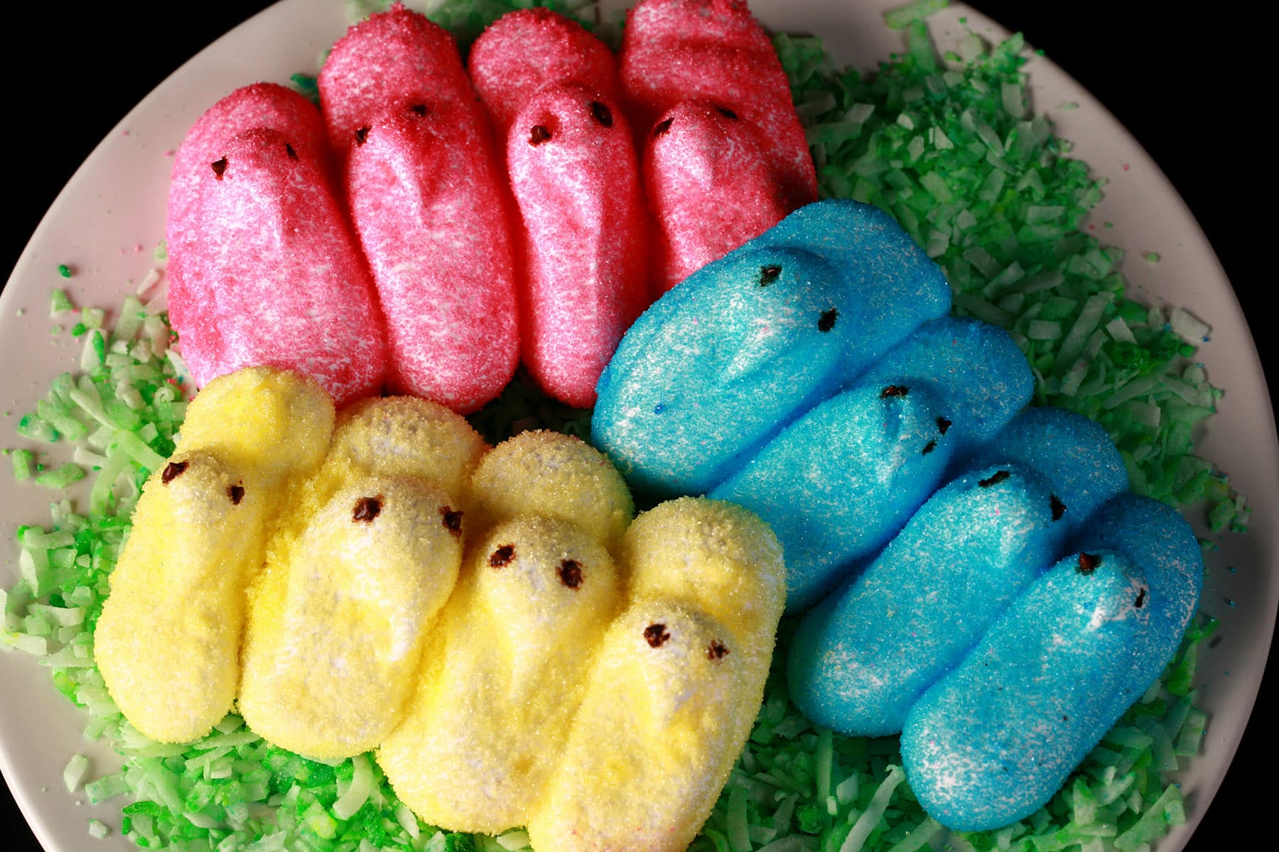 Pink, yellow, and blue chick shaped homemade marshmallow peeps on a bed of green coconut.