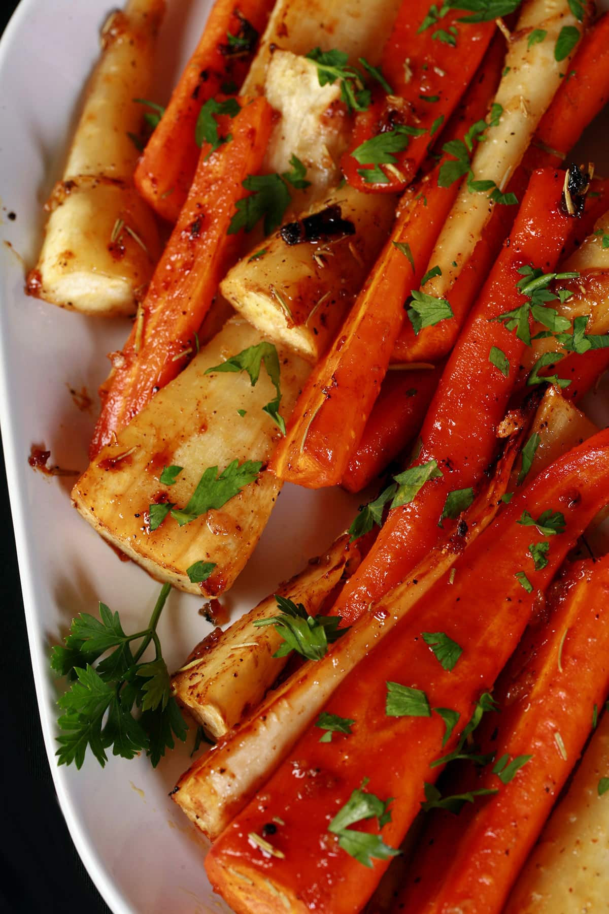 A platter of honey roasted carrots and parsnips, sprinkled with parsley.