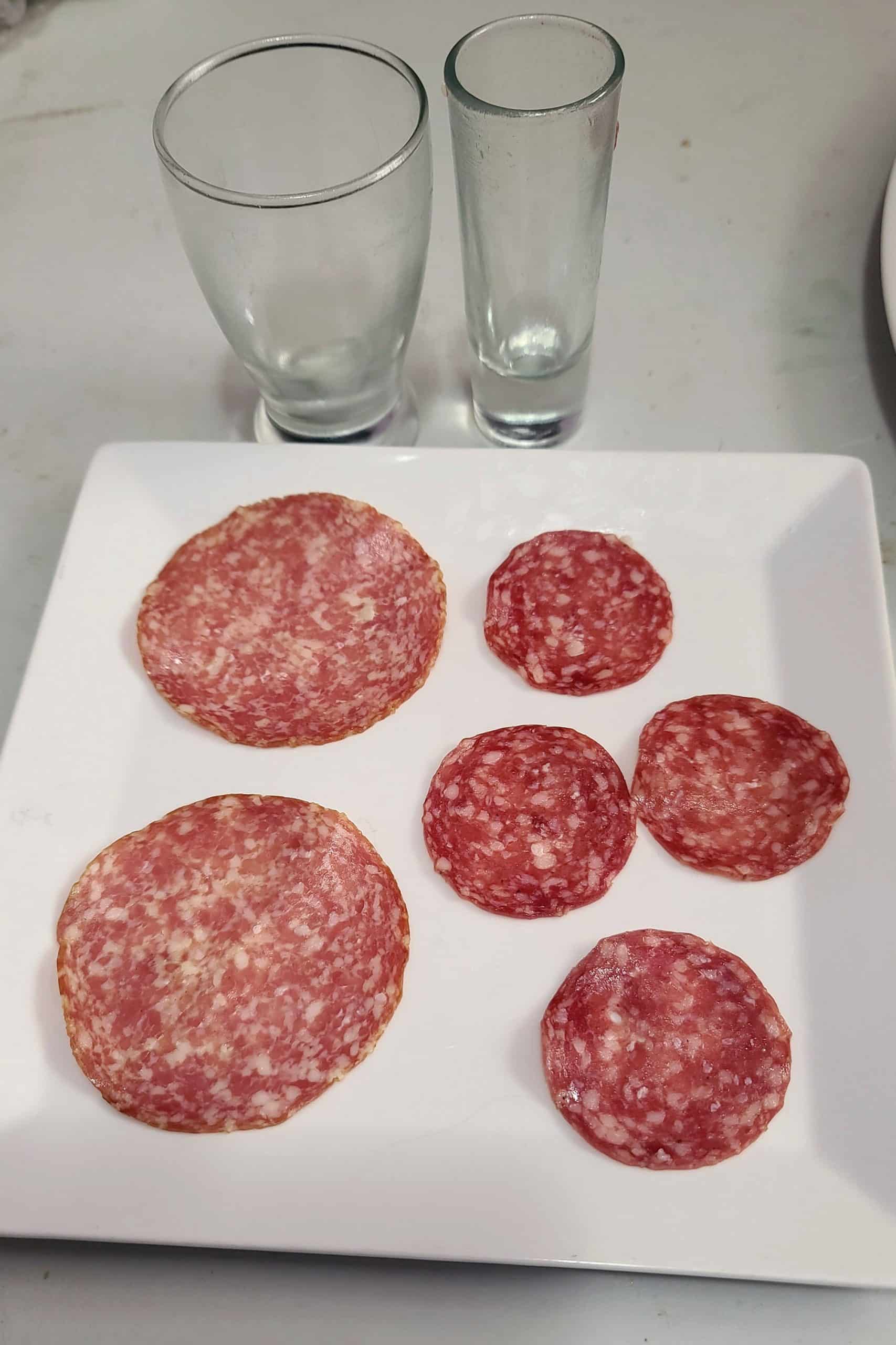 A plate with two sizes of salami and 2 small glasses.