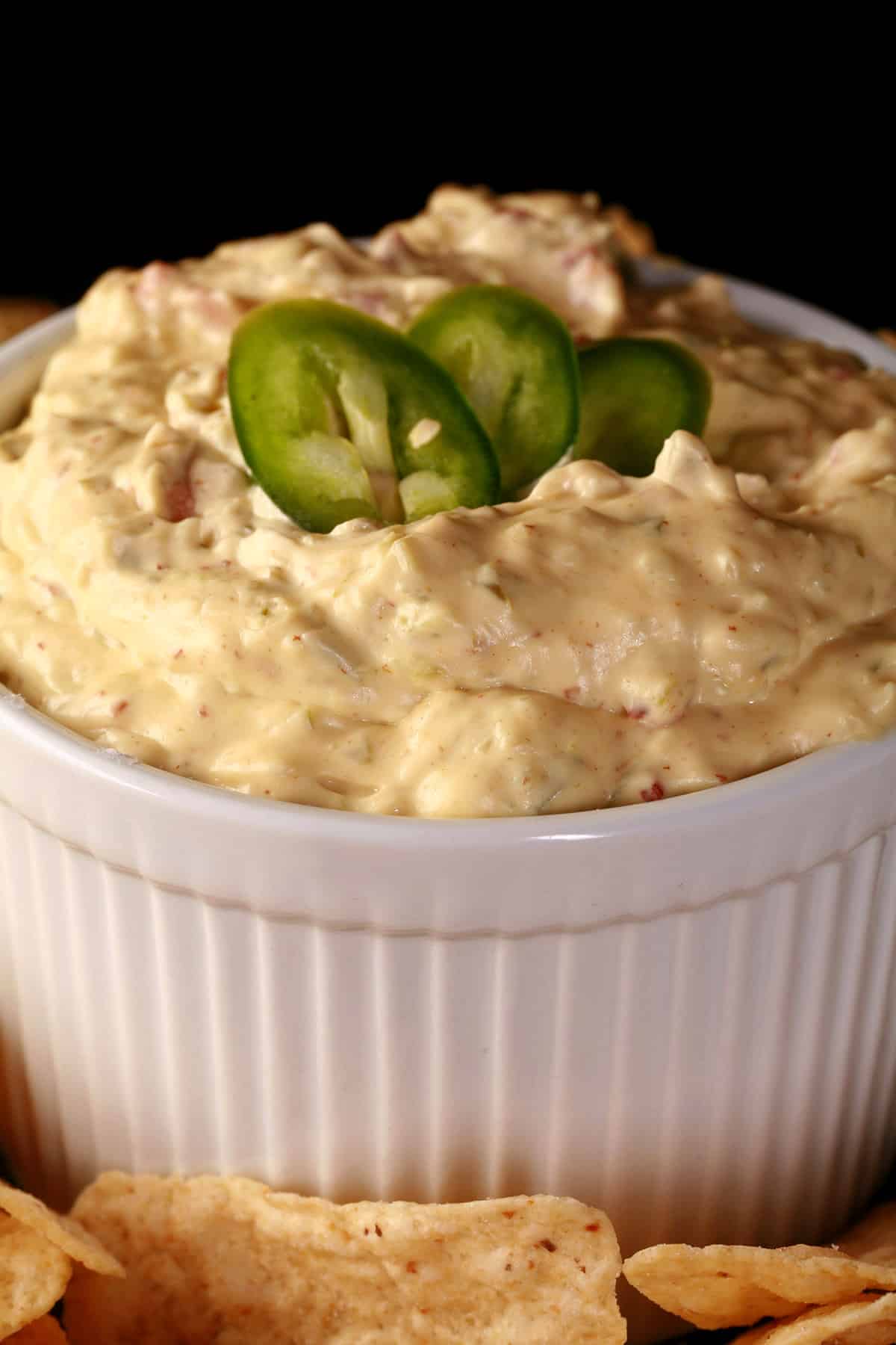 A ramekin of gluten free jalapeno dip, surrounded by corn chips and topped with sliced jalapenos.