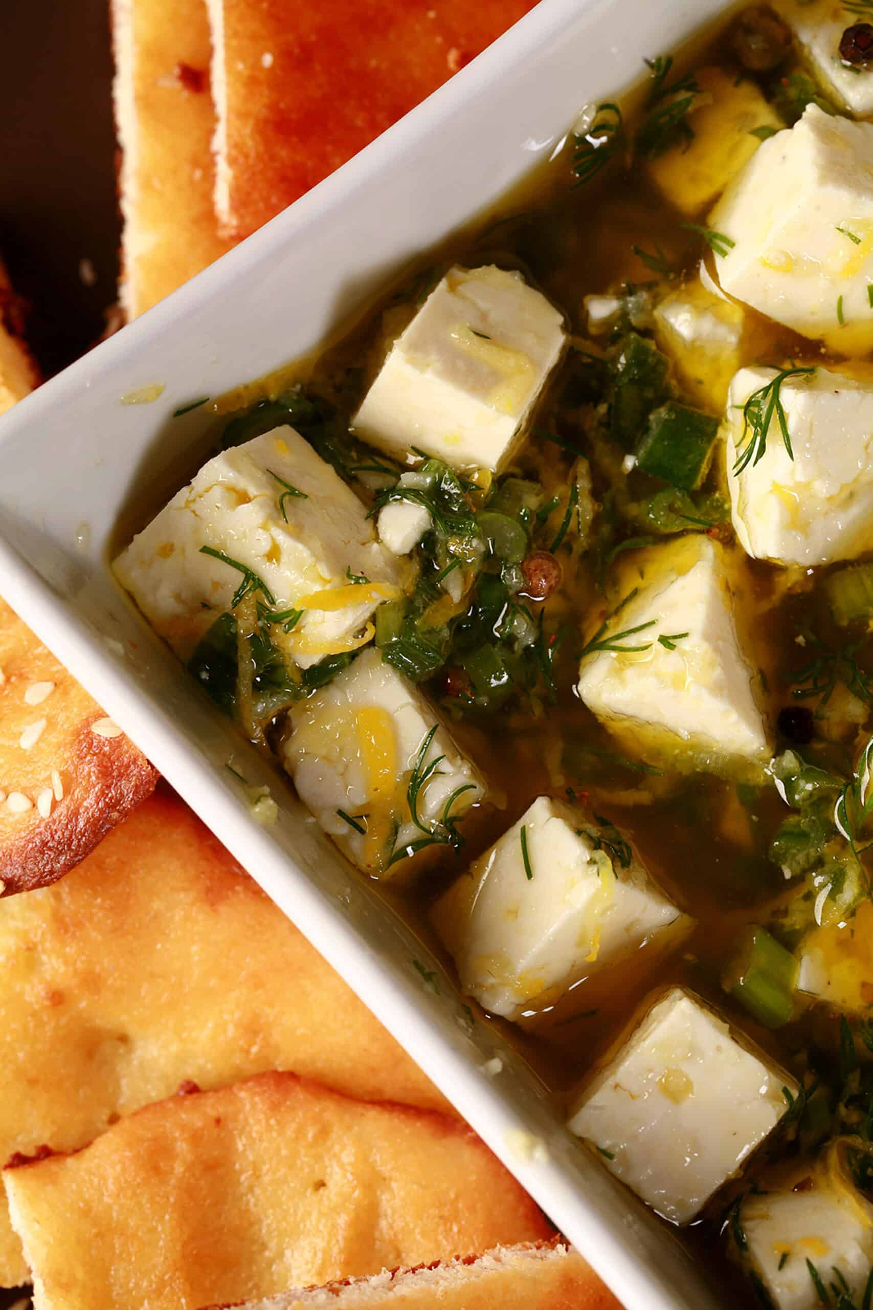 A bowl of lemon herb marinated feta surrounded with gluten free flatbread.