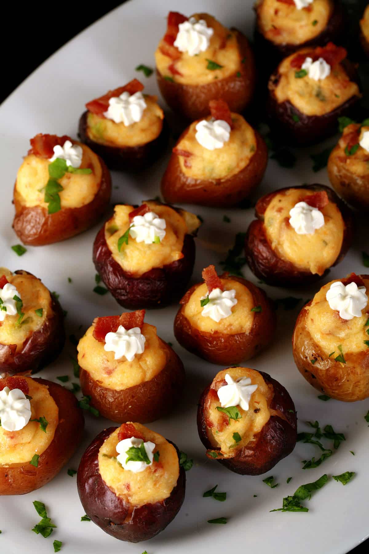 A party platter of loaded mini baked potatoes, topped with sour cream, bacon, and green onion.
