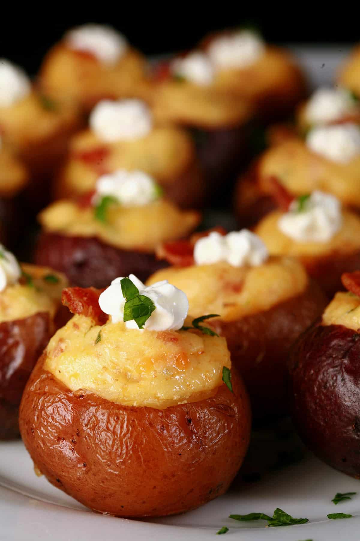 A party platter of mini loaded baked potatoes, topped with sour cream, bacon, and green onion.