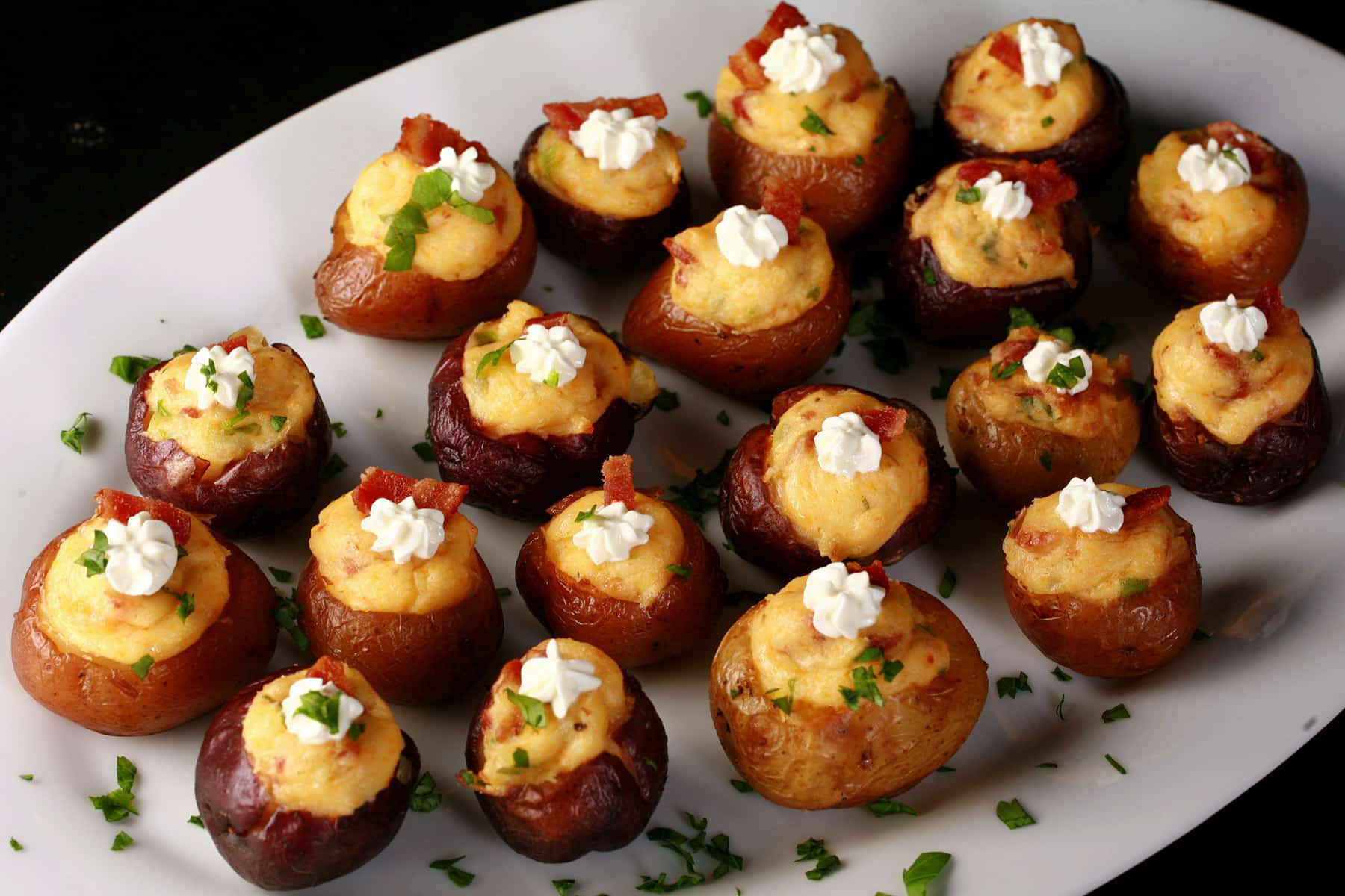 A party platter of loaded mini baked potatoes, topped with sour cream, bacon, and green onion.