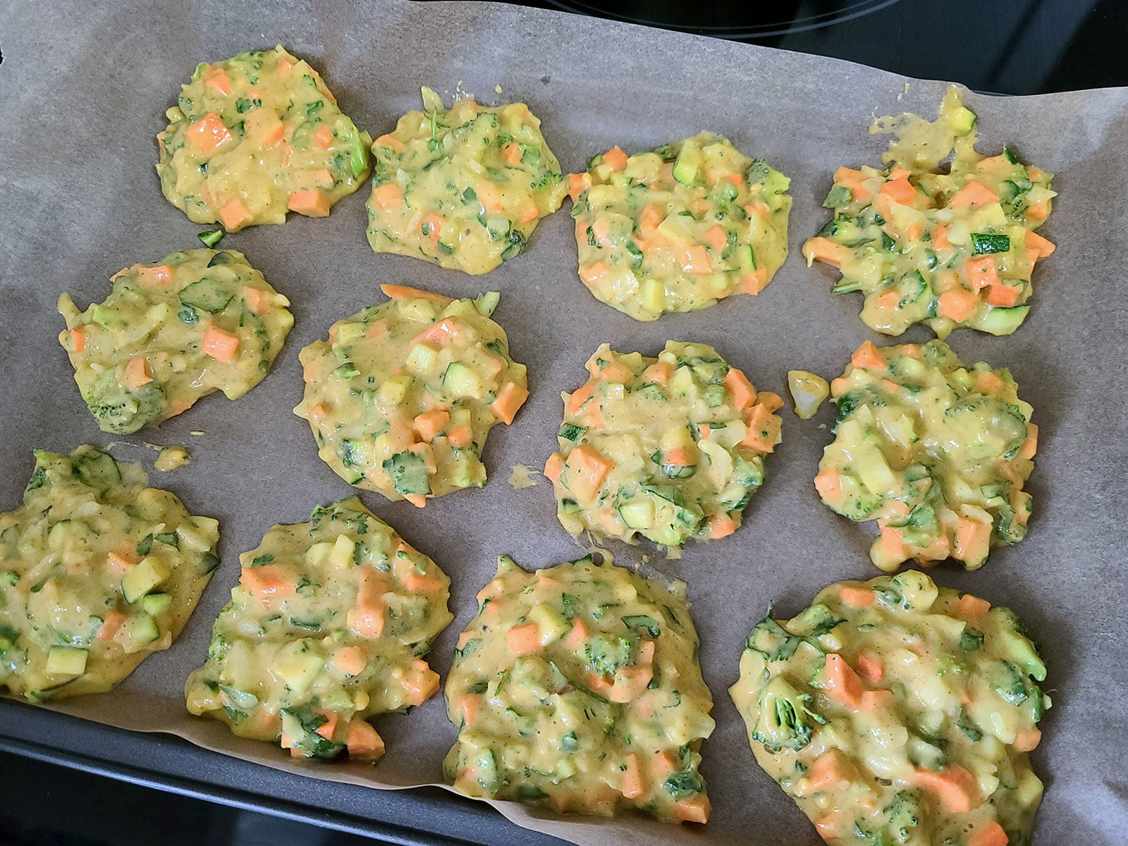 Spoonfuls of veggie pakora batter on a parchment lined baking sheet.