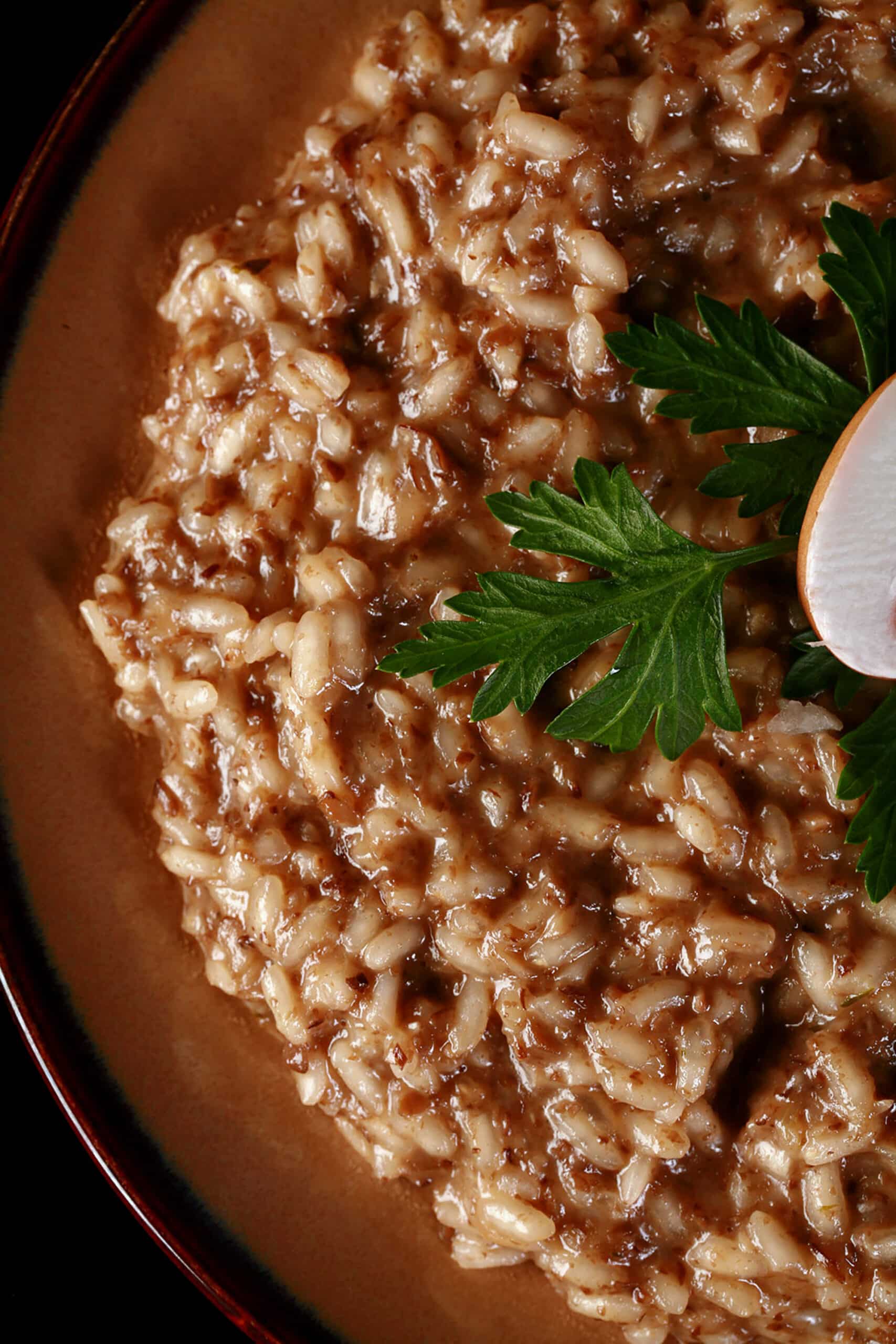 A plate of mushroom risotto, garnished with parsley leaves and sliced mushrooms.