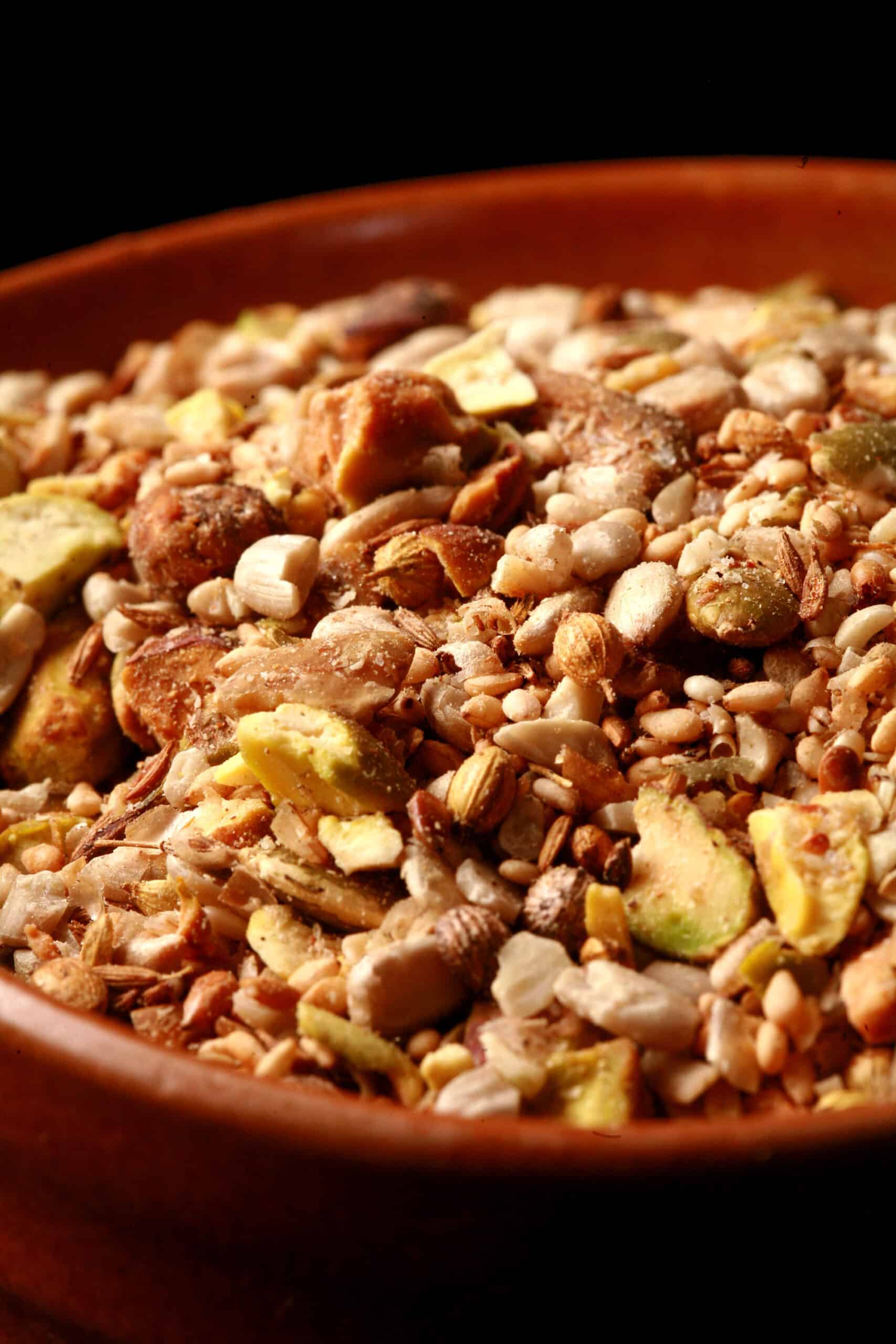 A small brown bowl of pistachio dukkag spice mix. Chunks of pistachios, coriander, sunflower seeds, and pumpkin seeds are visible.