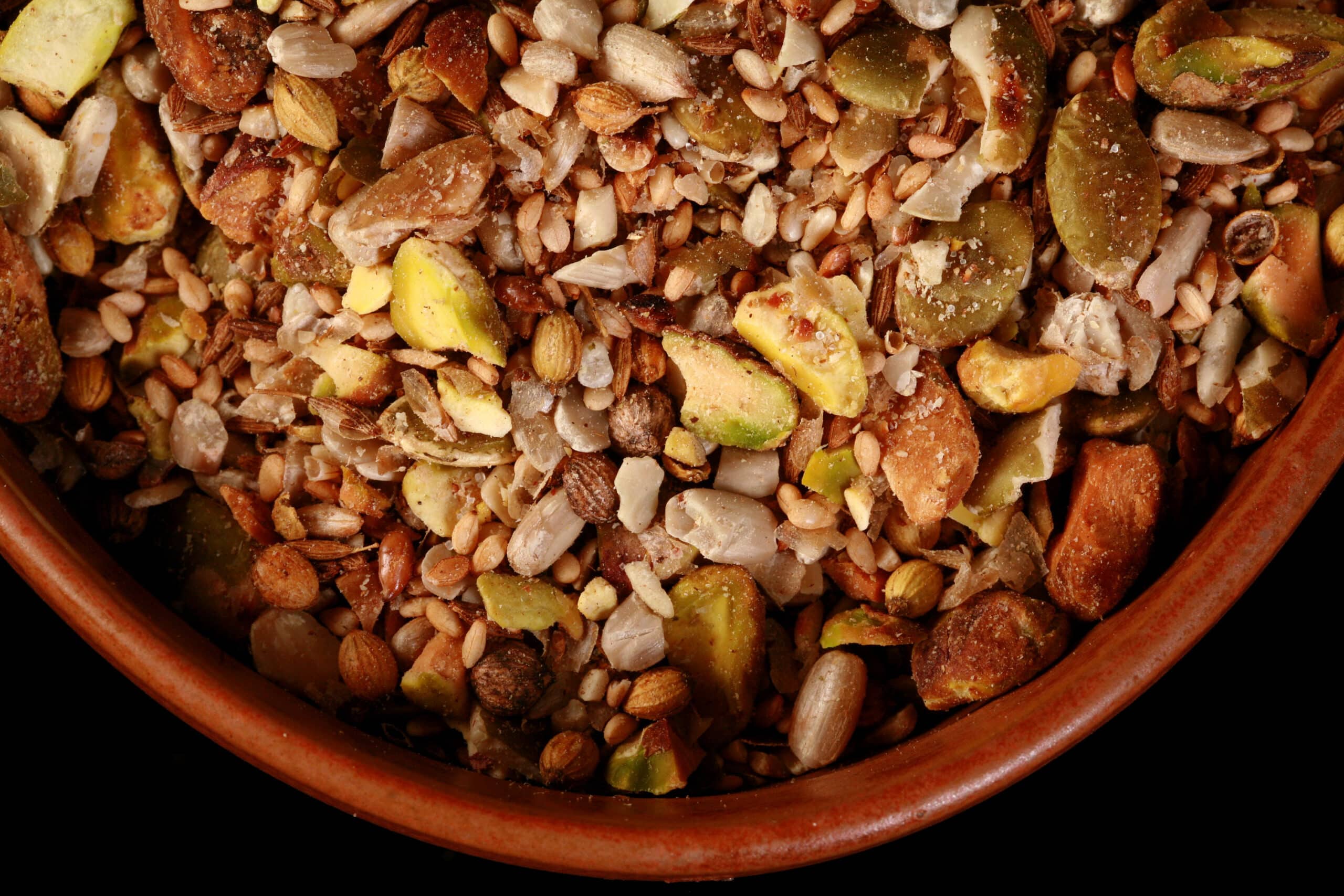 A small brown bowl of pistachio dukkag spice mix. Chunks of pistachios, coriander, sunflower seeds, and pumpkin seeds are visible.