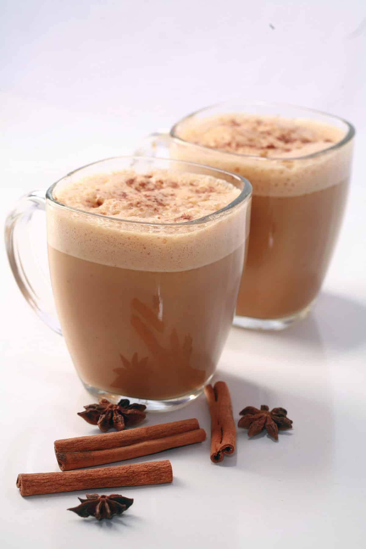 2 Pumpkin Chai Lattes in glass mugs, with cinnamon sticks and star anise around them.