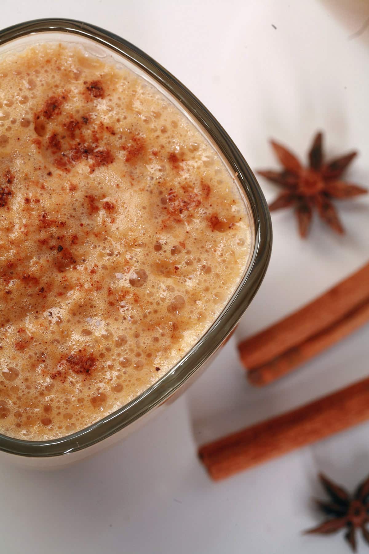A glass mug of pumpkin chai latte, with cinnamon sticks and star anise next to it.