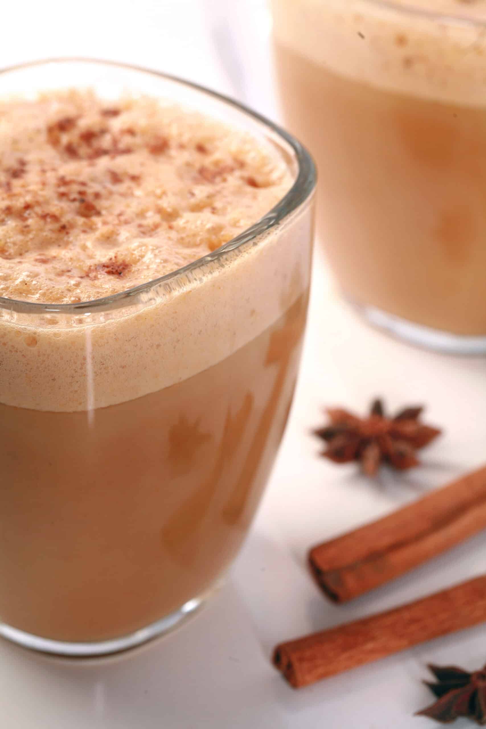 A glass mug of pumpkin chai latte, with cinnamon sticks and star anise next to it.