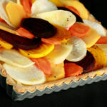 A close up view of a square root tart - a tart cooked in a square pan, with slices of a variety of root veggies arranged on top.