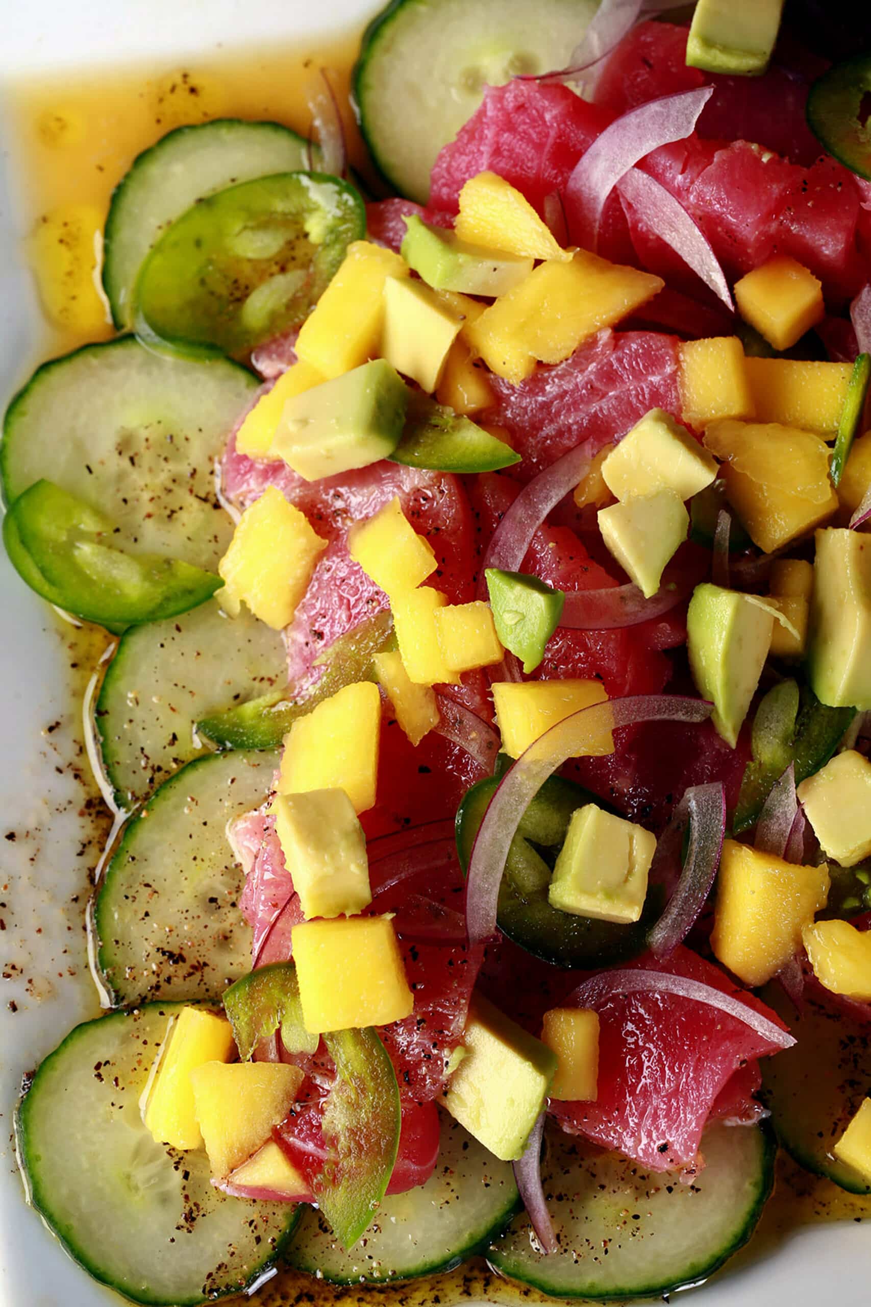 A close up photo of ahi tuna crudo, with mango, avocado, jalapenos, and a citrus vinaigrette, served over cucumber slices.