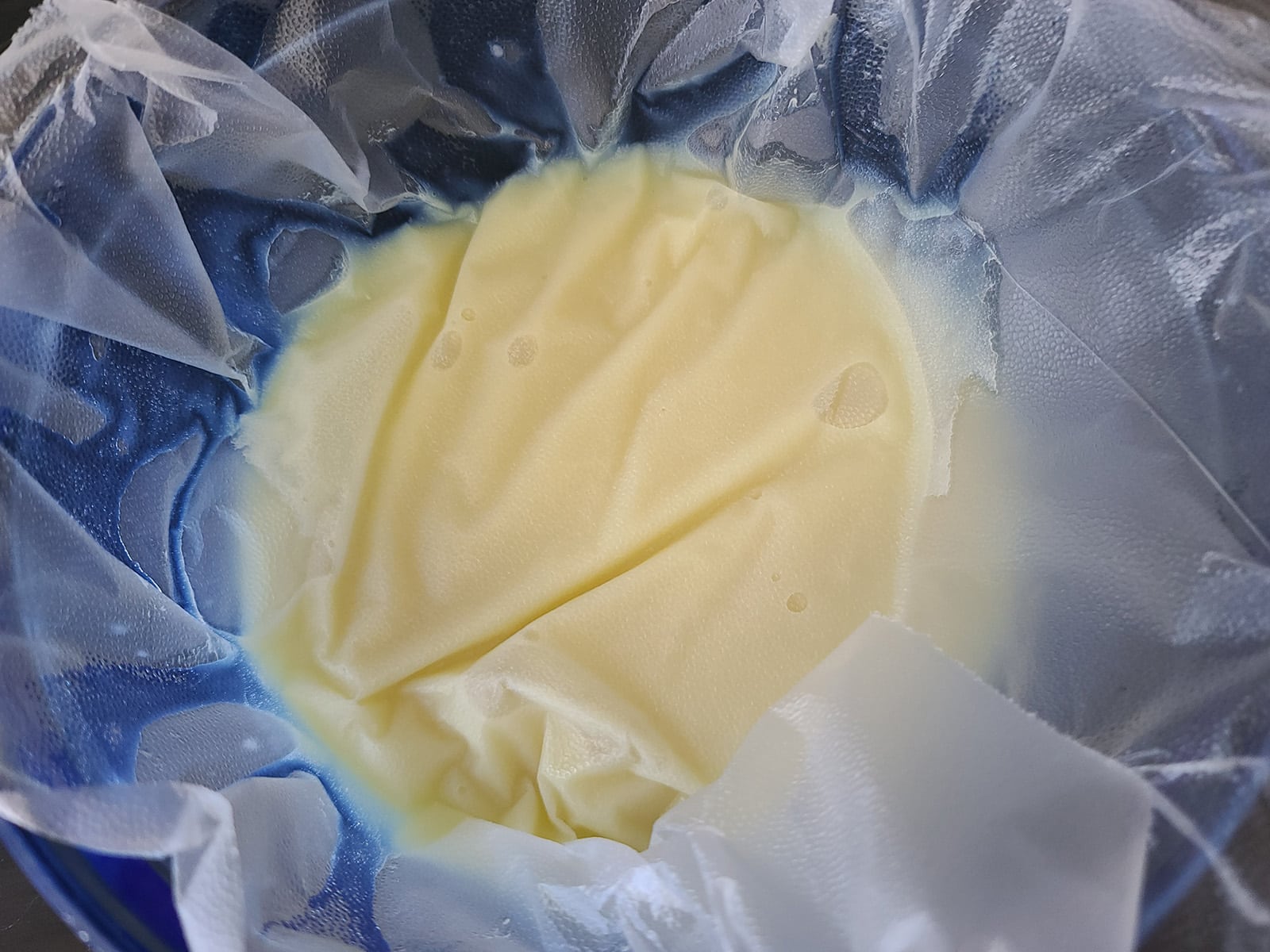 A bowl of melted white chocolate ganache with plastic wrap right against the surface.